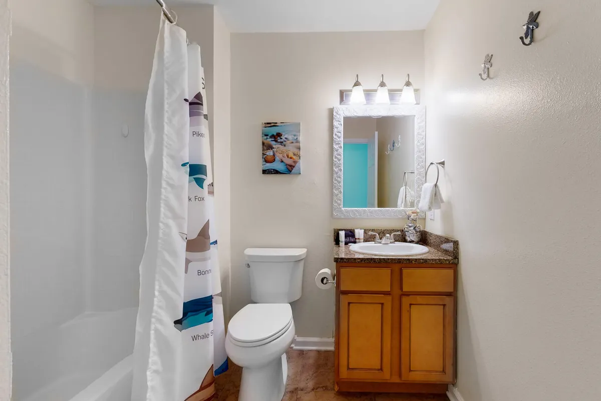 A light-filled bathroom with a modern vanity, elegant sink, framed mirror, inviting bathtub, and a colorful shower curtain. The space is spotless and designed for rejuvenation.