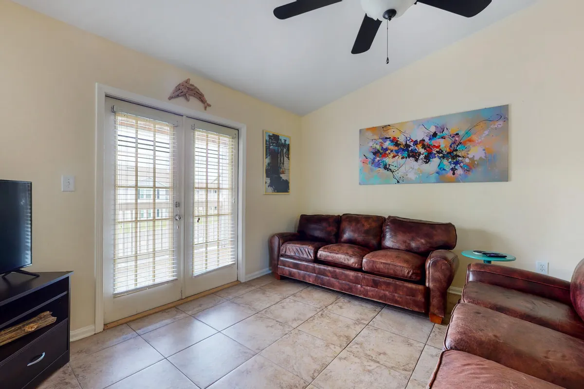 A bright, open-plan living room featuring comfortable sofas, vibrant artwork on the wall, and large sliding doors that let in plenty of natural light. The doors open toward the balcony, visually connecting indoor relaxation with the outdoor experience.