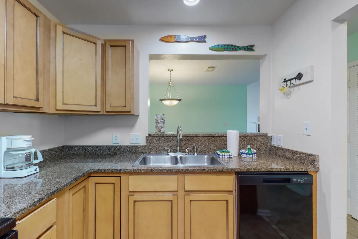 An inviting kitchen scene with granite countertops, a double stainless steel sink, wooden cabinetry, and decorative fish wall art. The layout suggests a space ideal for preparing meals, cleaning, and casual dining in a homey environment.
