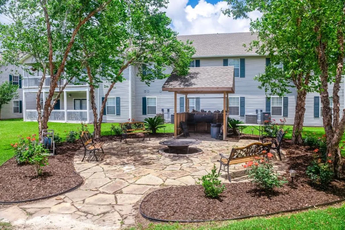 The image shows a covered barbecue area with a central fire pit, surrounded by benches and lush greenery. This setting is ideal for outdoor grilling, social gatherings, and relaxing evenings spent connecting with neighbors or family.